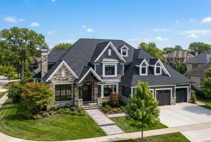 Aerial view of a large stone and shingle suburban house with multiple gables, dormers and metal accent roofing