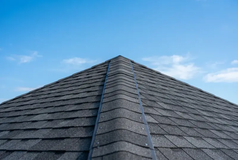 Close-up along the ridge of a new dark shingle roof showing a continuous ridge vent running the length of the hip, against a clear sky