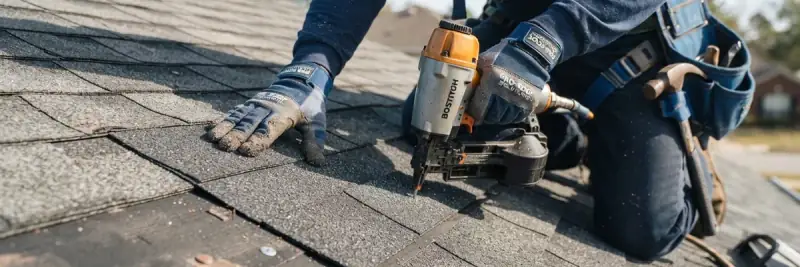 Close-up of a roofer driving fasteners through a course of asphalt shingles with a pneumatic nail gun